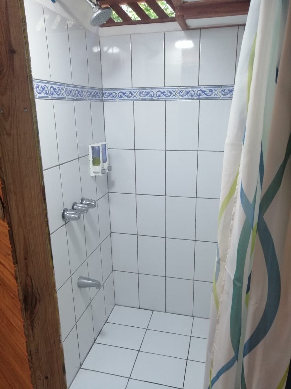 A shower area with white tiled walls, a showerhead, and a curtain.