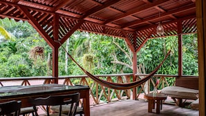 A wooden deck with a table and chairs, a hammock, and a view of lush greenery. - Chalet Y Cabinas Hibiscus (Cahuita)