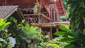A wooden house with a balcony, surrounded by lush greenery. - Chalet Y Cabinas Hibiscus (Cahuita)