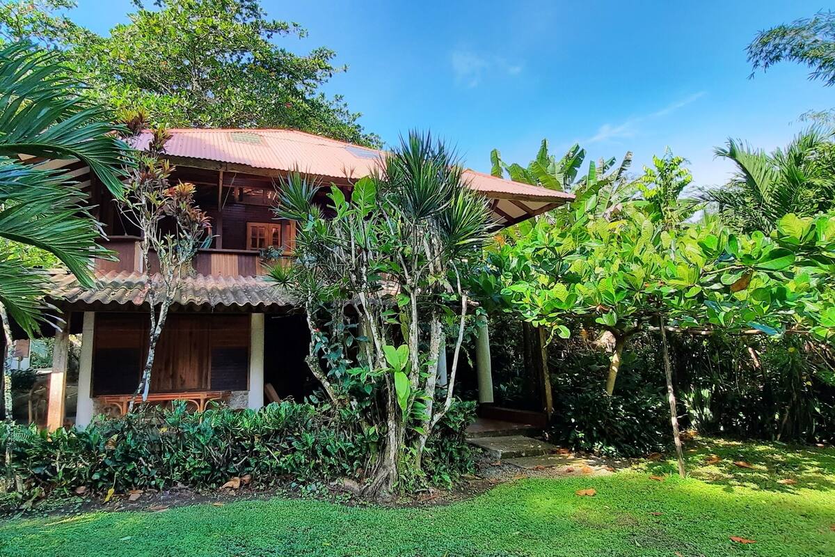 Une maison en bois à deux étages, entourée d’une végétation luxuriante.