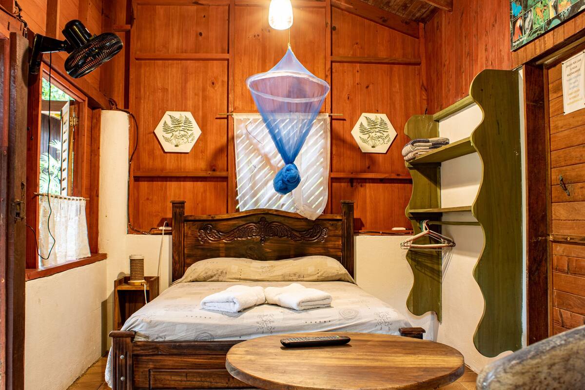 Une pièce en bois avec un lit, une table ronde, un luminaire suspendu et une étagère fixée au mur.
