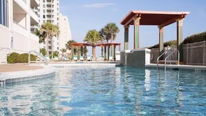 A swimming pool with clear water, surrounded by a building with balconies and a covered area with chairs. - Pearl 1001 Completely renovated from floor to ceiling! Super clean!  (Navarre)