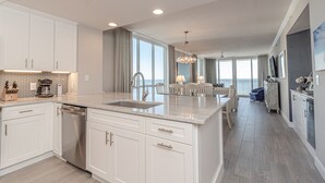 A modern kitchen with white cabinetry, a large island, and a view of the ocean. - Pearl 1001 Completely renovated from floor to ceiling! Super clean!  (Navarre)
