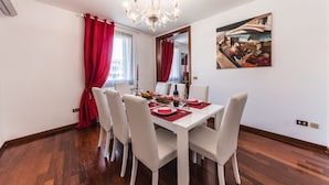 Une salle à manger avec une table blanche dressée pour quatre personnes, des rideaux rouges, un lustre et un tableau accroché au mur.