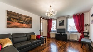 Un salon avec un canapé noir, un téléviseur et un tableau accroché au mur.