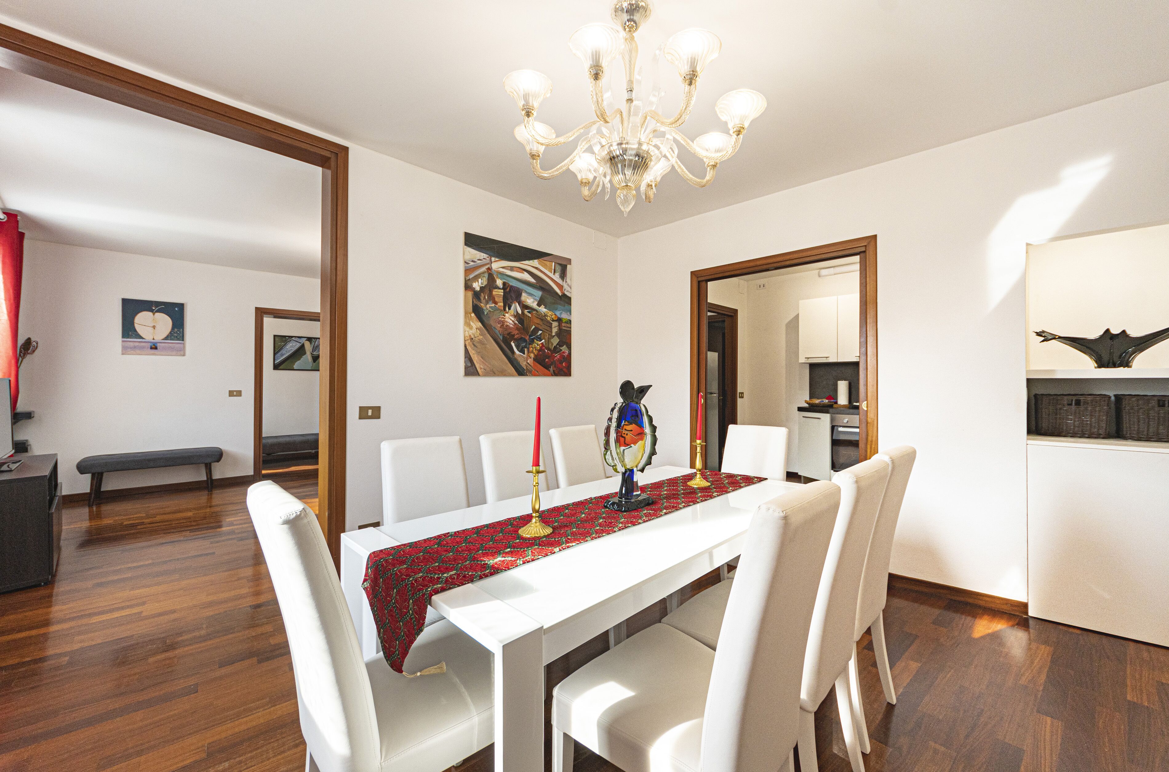 A dining area with a white table, red tablecloth, and candles. There are white chairs around the table. A chandelier hangs from the ceiling.
