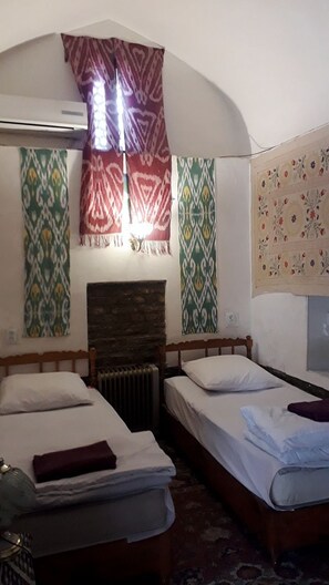 A room with two beds, a radiator, patterned curtains, and a wall-mounted air conditioner. - Mekhtar Ambar (Bukhara)