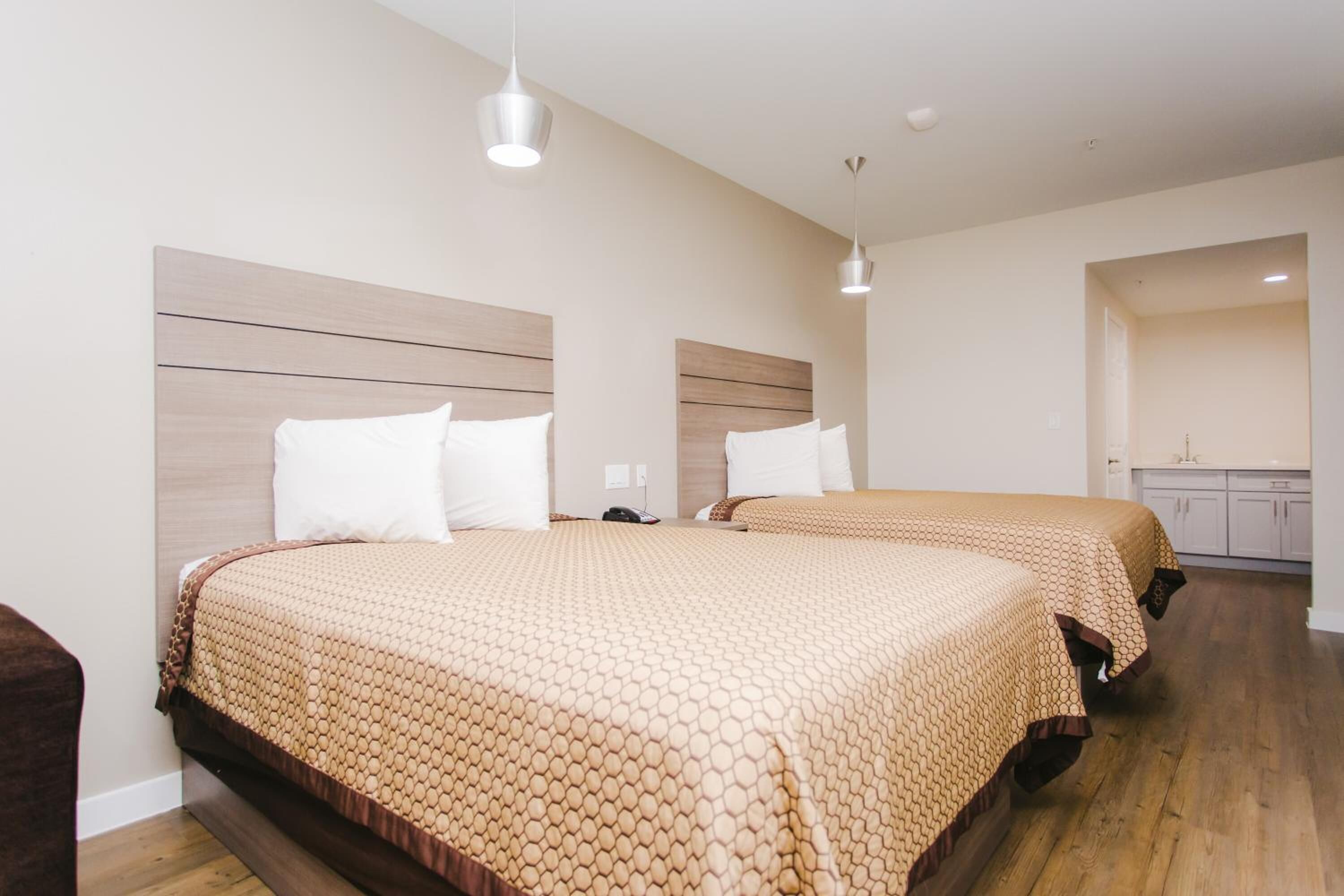 A hotel room with two beds, wooden headboards, and a small kitchenette.