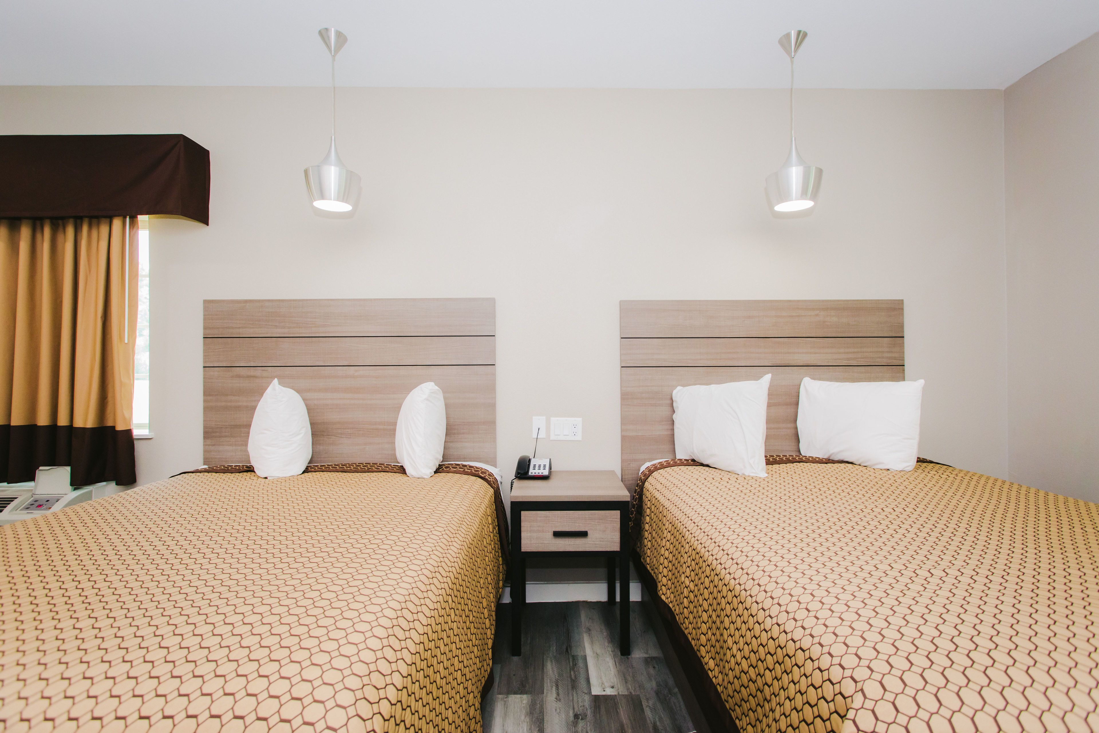 Quarto de hotel com duas camas, mesa de cabeceira, telefone e janela com cortinas.