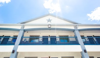 Un edificio con una estrella destacada en la fachada, un balcón con barandas azules y un cielo despejado al fondo.