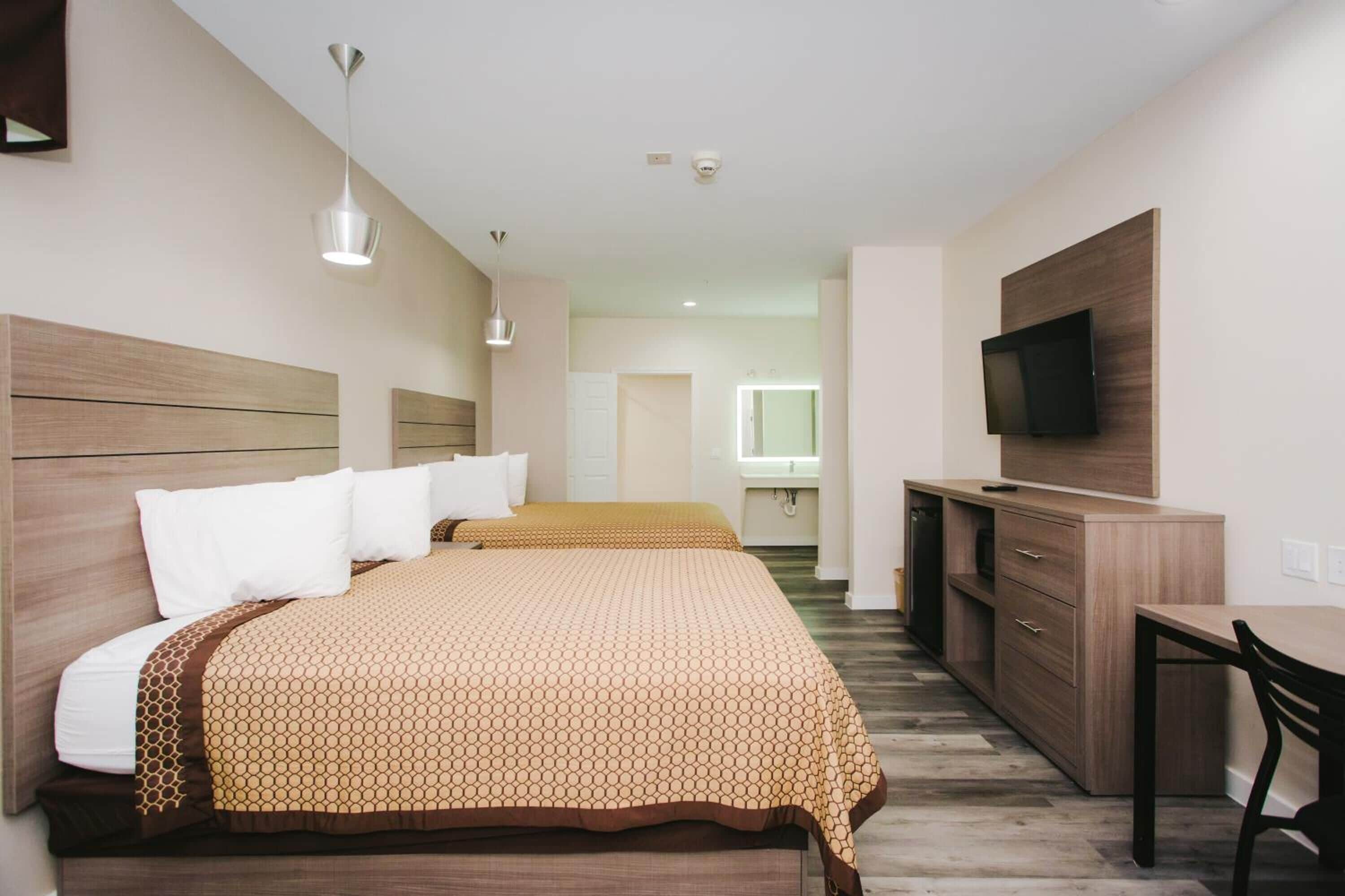 A hotel room with two beds, a desk, a television, and a mirror.