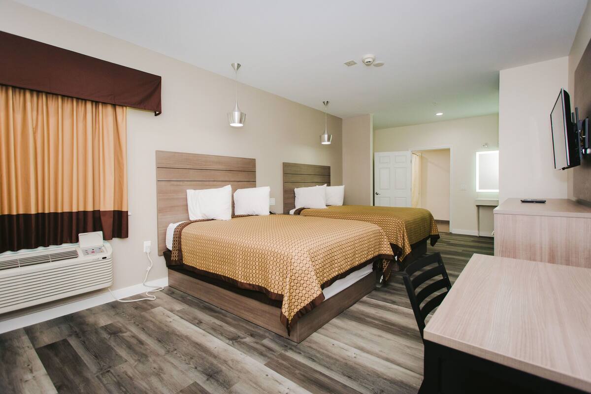 A hotel room with two beds, a desk, and a TV.