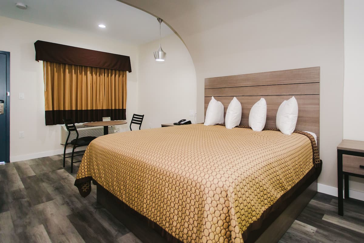 A hotel room with a large bed, a desk, a chair, and a window with curtains.