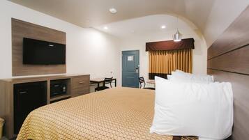 Habitación de hotel con una cama grande, un televisor de pantalla plana montado en la pared, un escritorio con una silla y una ventana con cortinas.