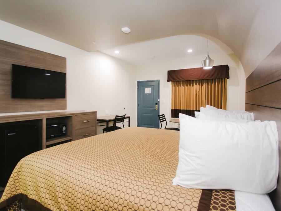 Habitación de hotel con una cama grande, un televisor de pantalla plana montado en la pared, un escritorio con una silla y una ventana con cortinas.