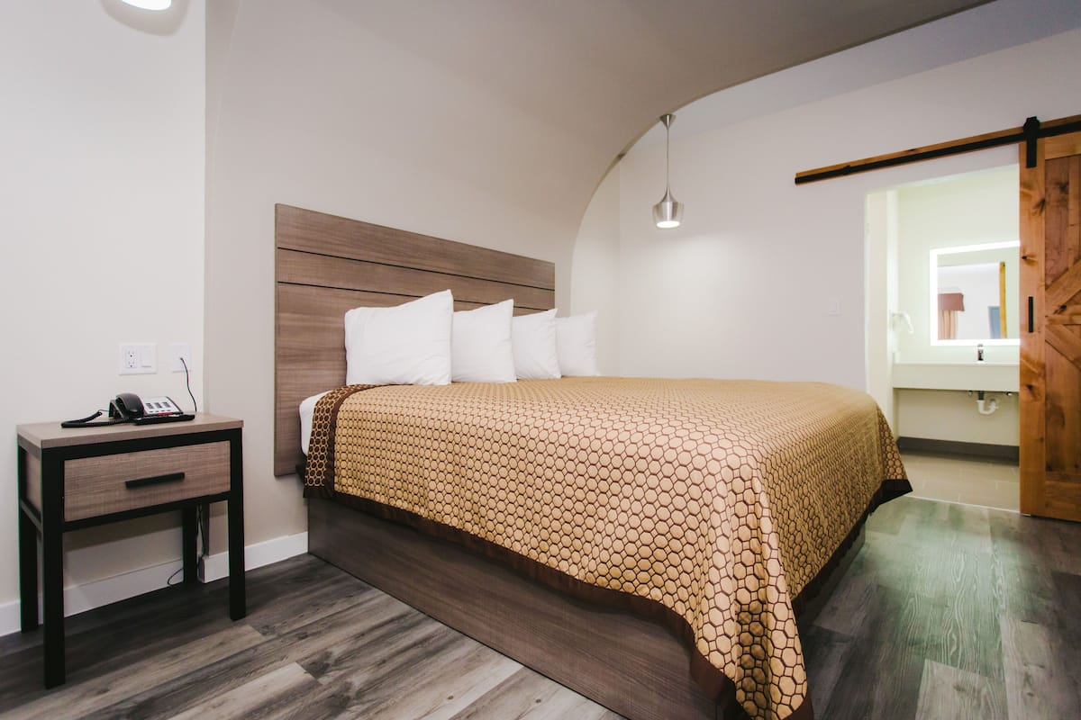 A bedroom with a wooden headboard, a bed with a patterned bedspread, a bedside table with a phone, and a hanging light fixture.