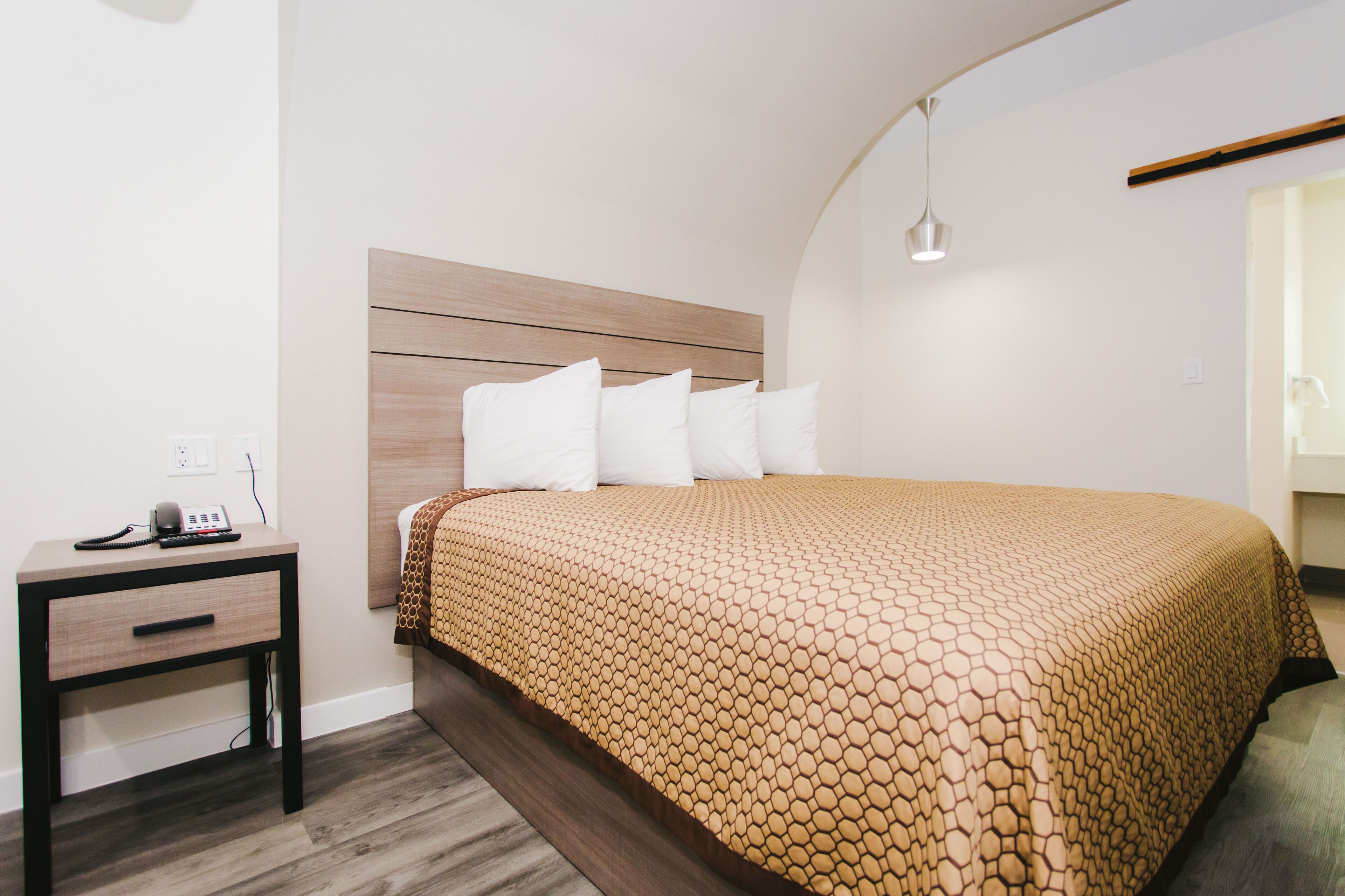 Quarto com cabeceira de madeira, cama com colcha estampada, mesa de cabeceira com telefone e luminária pendente.