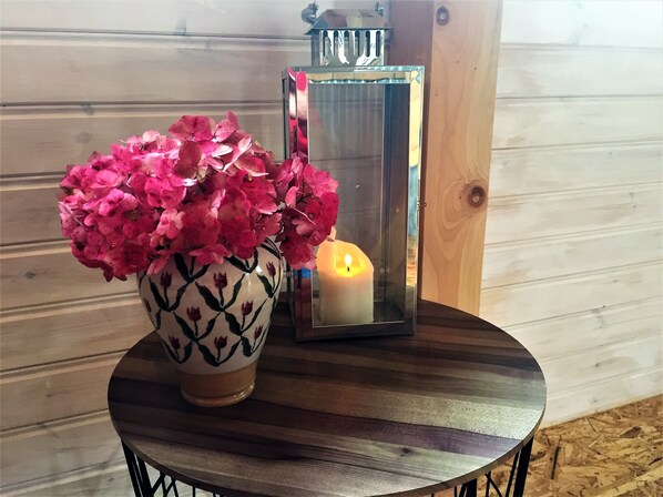 A round wooden table with a vase of pink flowers and a lit candle.