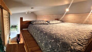 A bedroom with a large bed, wooden walls, a window, and a wooden staircase.