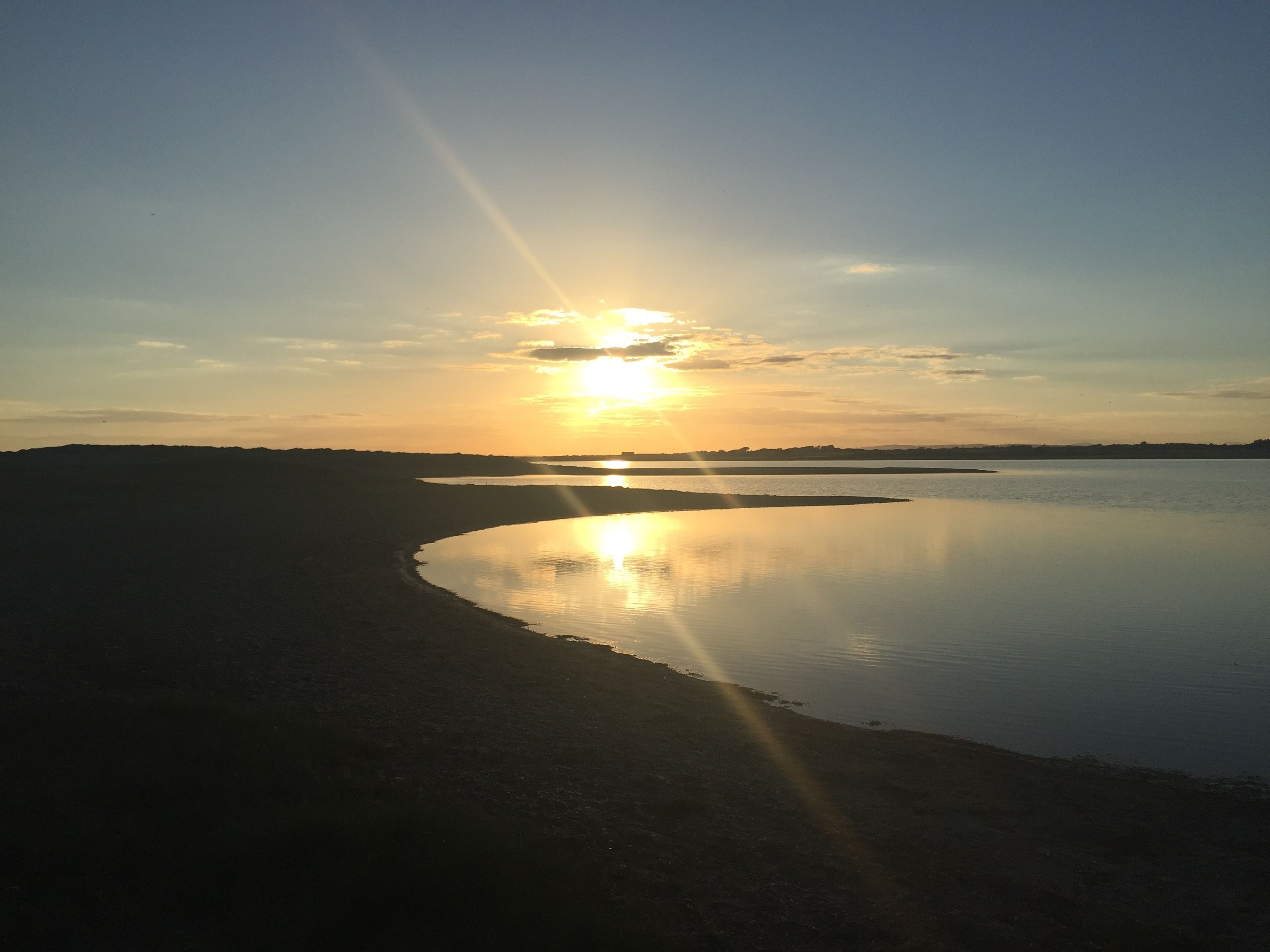 Un atardecer sobre una masa de agua tranquila con una costa curva.