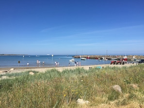 A coastal beach with boats, a tractor, and people by the water. - St Awaries (Lady's Island)