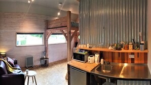 Una habitación compacta con piso de madera, un sofá, una mesita, una kitchenette con pileta y un ventanal.
