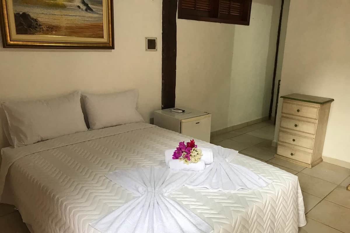 Een net opgemaakt bed met decoratieve handdoek en bloemen, een nachtkastje, een bijzettafeltje en een kleine dressoir in een hotelkamer.