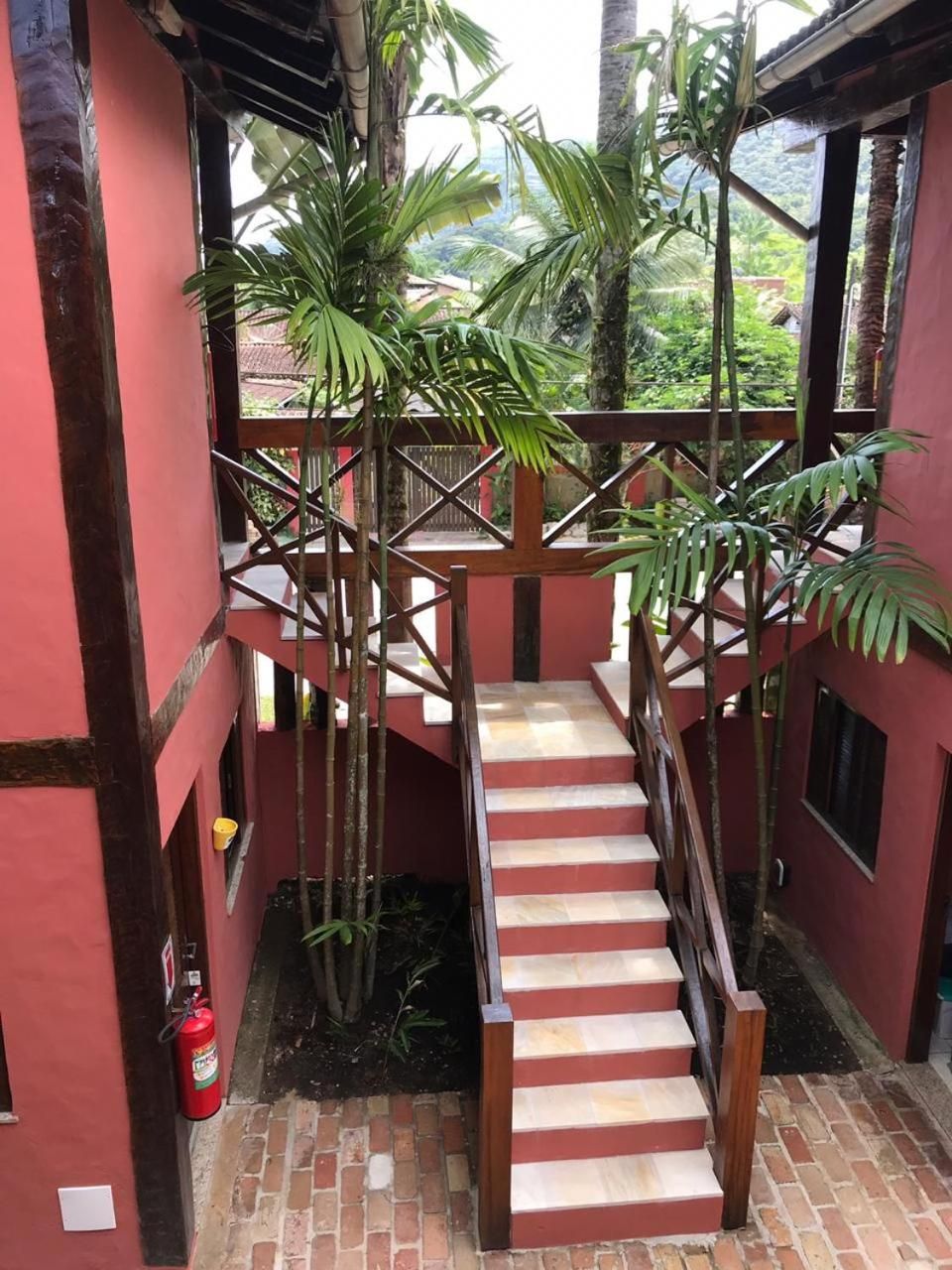 A staircase with a wooden handrail leading to a balcony, surrounded by red walls and potted plants.