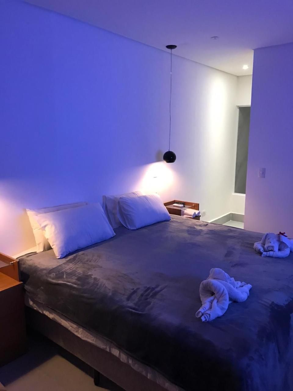Een slaapkamer met een bed, kussens, een nachtkastje en een hanglamp.