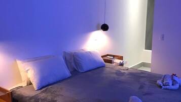 Een slaapkamer met een bed, kussens, een nachtkastje en een hanglamp.