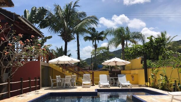 Une piscine dont les bords sont recouverts de carreaux, entourée de chaises longues et de parasols, avec des palmiers et une montagne en arrière-plan.