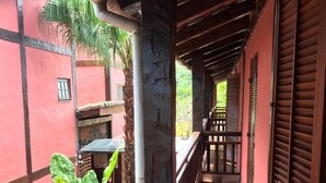 Un balcon en bois offrant une vue sur un immeuble rouge et un palmier.