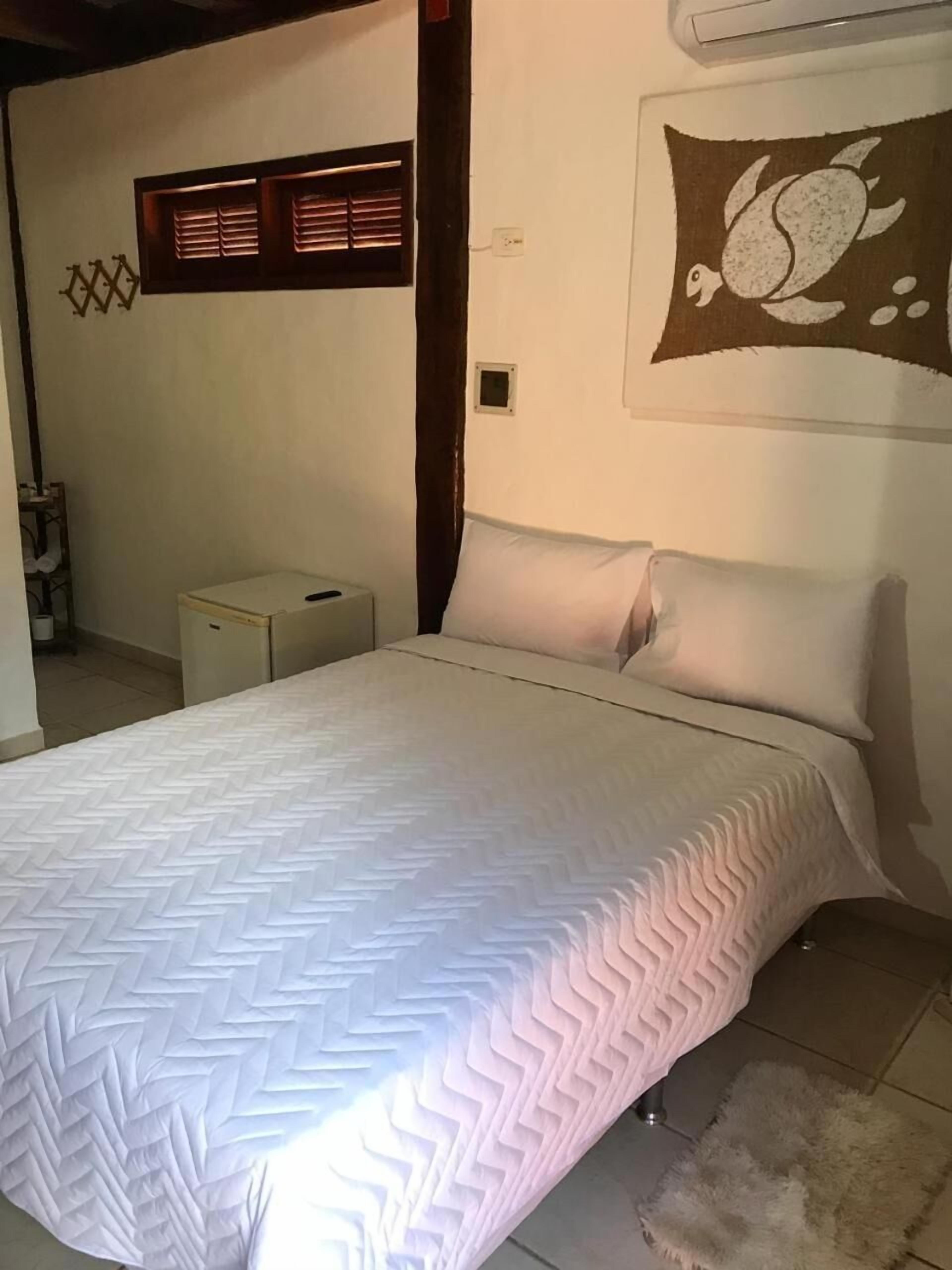 A bedroom with a bed, a small bedside table, a wall-mounted air conditioner, and a decorative wall piece.