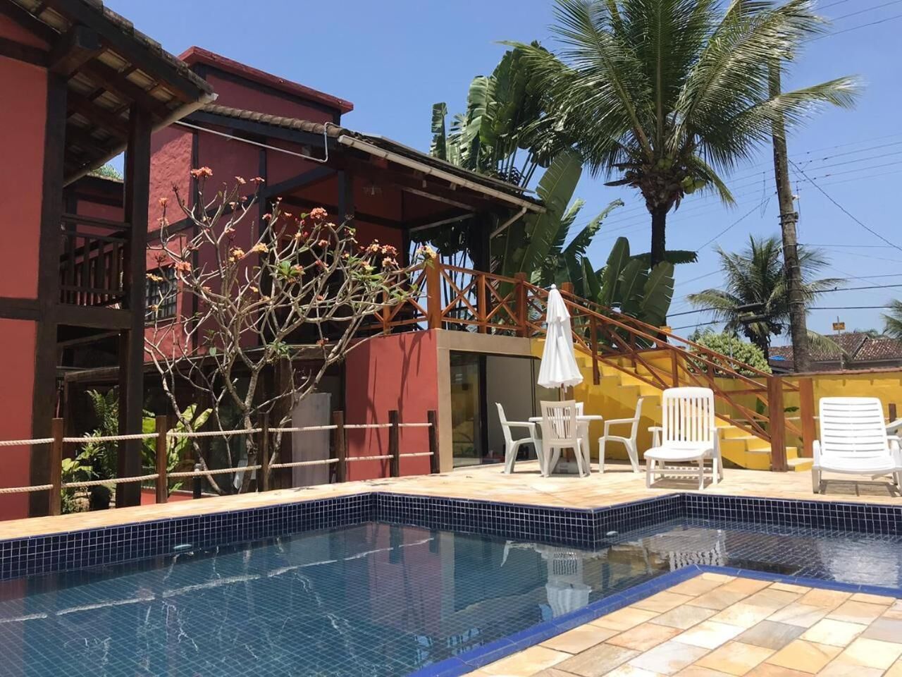 Una piscina con bordes de azulejos, rodeada por una cubierta de madera y sillas de descanso blancas.