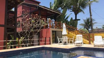 Una piscina con bordes de azulejos, rodeada por una cubierta de madera y sillas de descanso blancas.