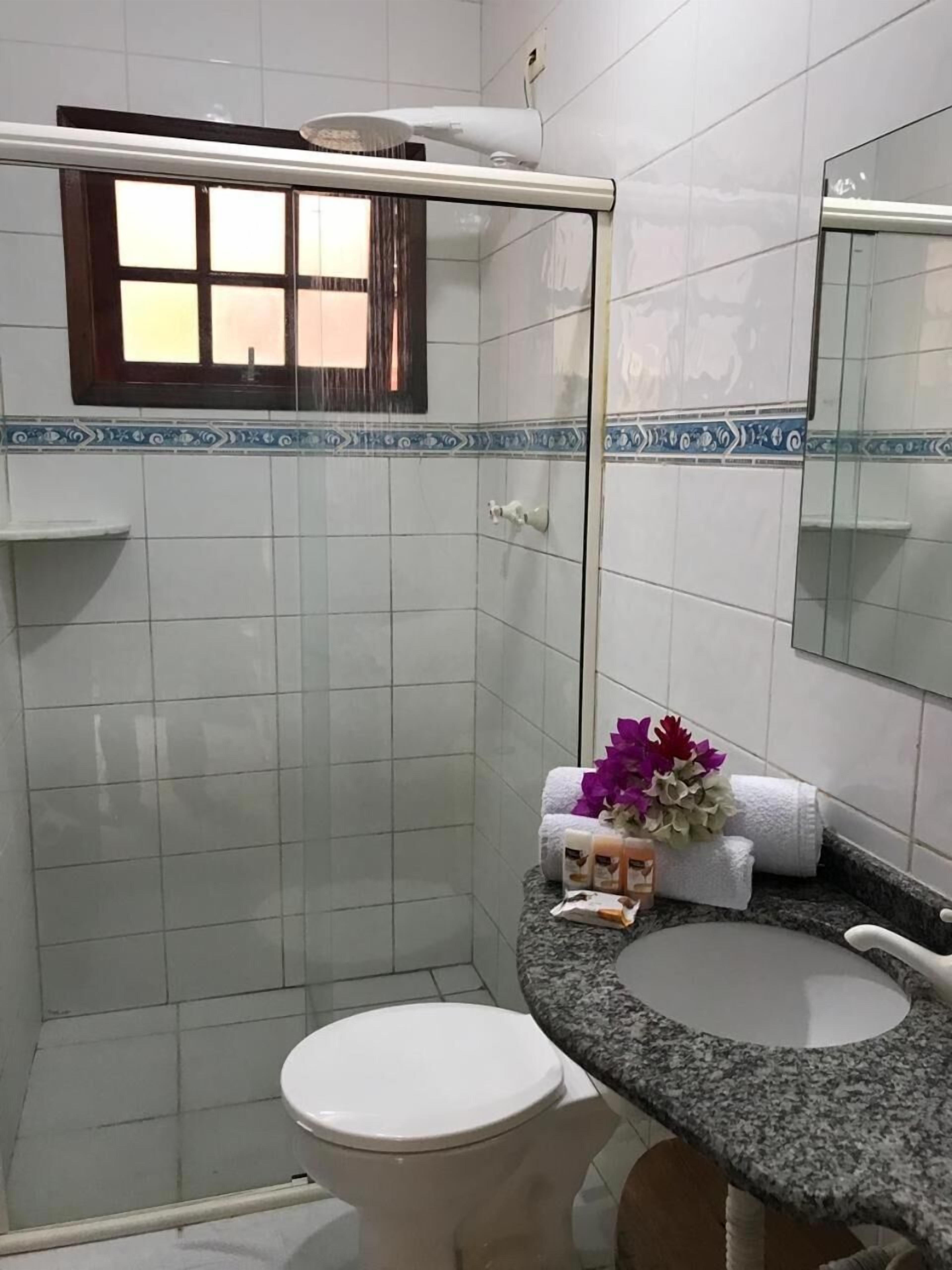 A bathroom with white tiled walls, a shower area, a toilet, a sink with a granite countertop, and a mirror.
