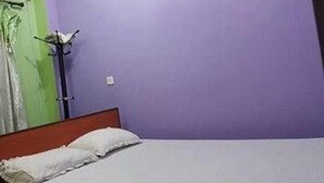 Una habitación con una cama, una puerta verde y una pared morada.