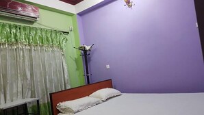 Un dormitorio con cama, pared verde, pared de acento púrpura y una ventana con cortinas verdes.