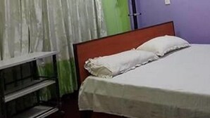 Una cama individual con colchón y almohadas blancos, cabecera de madera y una estantería metálica.