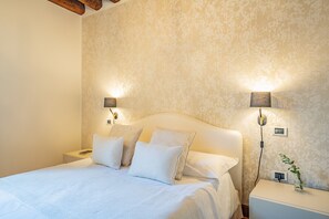 A bedroom with a bed, two bedside lamps, a nightstand, and a wall-mounted outlet. - Ca' Del Monastero 6 Collection (Venice)