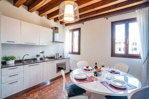 A modern kitchen with white cabinets, a dining table set for two, and a window with curtains. - Ca' Del Monastero 6 Collection (Venice)