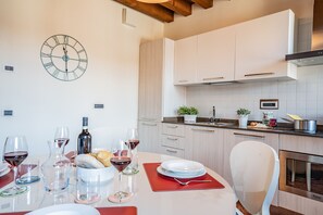 A modern kitchen with white cabinets, a clock, and a dining area set with wine glasses and plates. - Ca' Del Monastero 6 Collection (Venice)