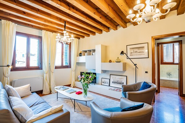 A living room with a wooden ceiling, a white sofa, a coffee table, and a chandelier. - Ca' Del Monastero 6 Collection (Venice)