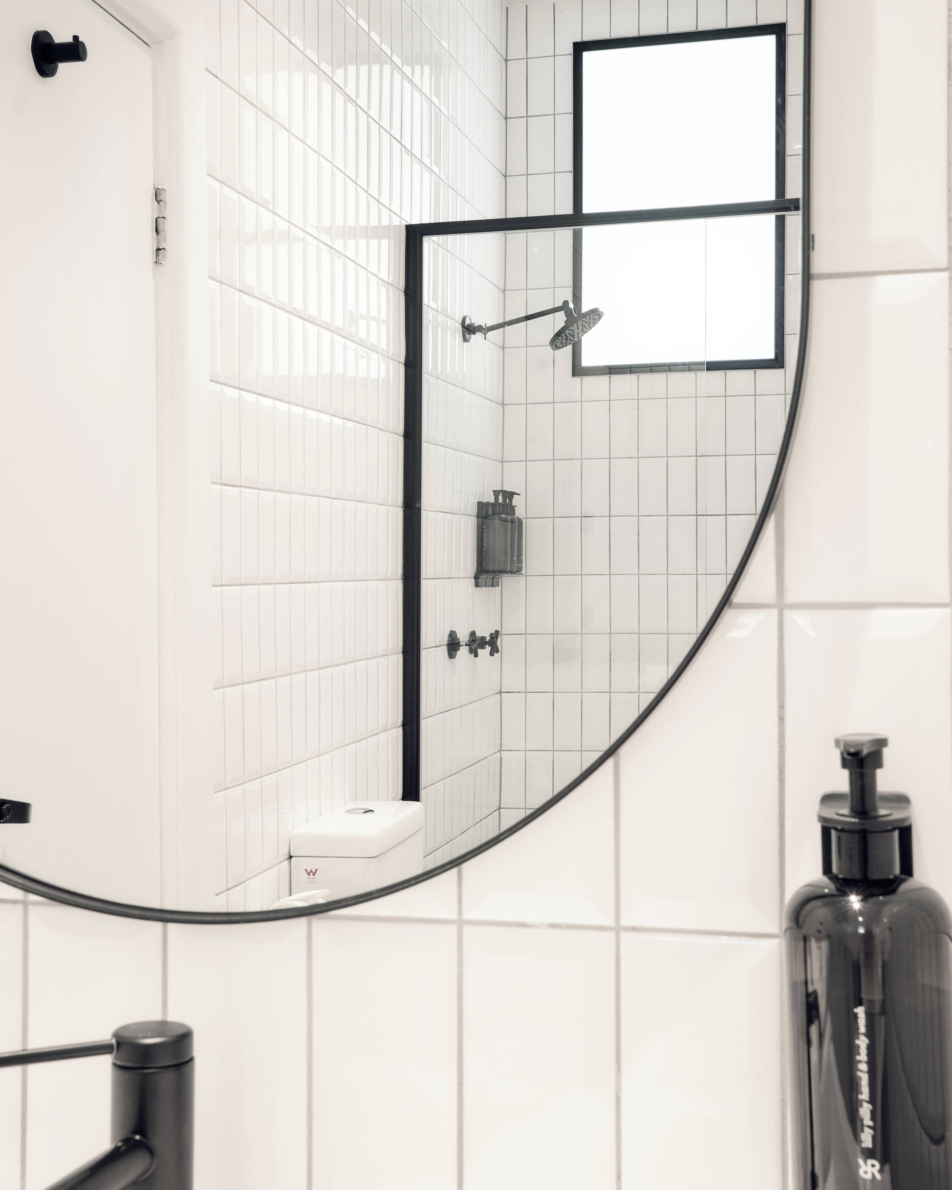Een badkamer met witte betegelde wanden, een douchegedeelte en een grote spiegel.