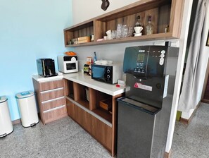 A compact kitchenette with a refrigerator, microwave, coffee maker, and a shelf with glassware and bottles. - HOUSE INN (Jinning)