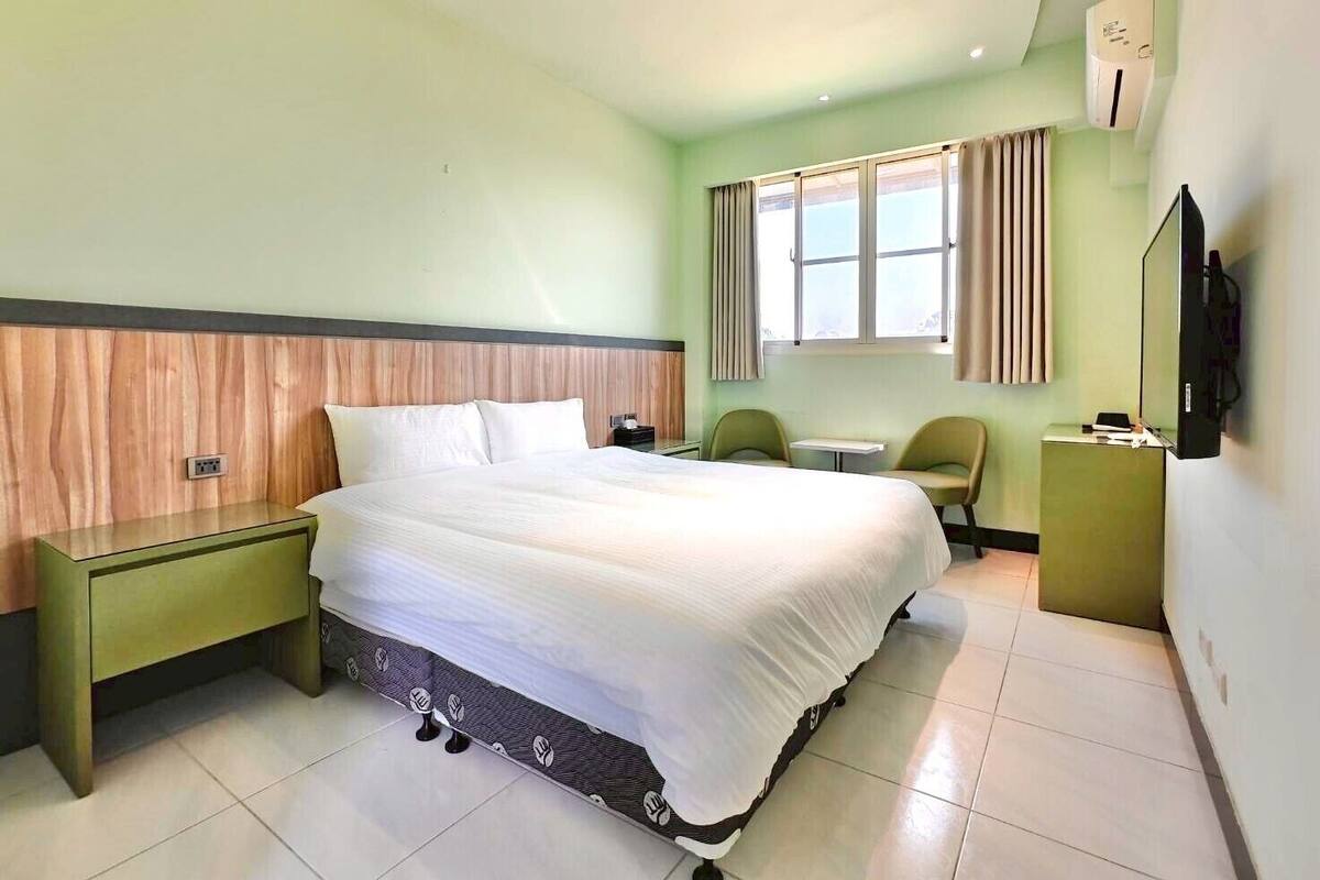 Une chambre d’hôtel équipée d’un lit, d’un bureau, d’une chaise, d’une télévision et d’une fenêtre avec des rideaux.