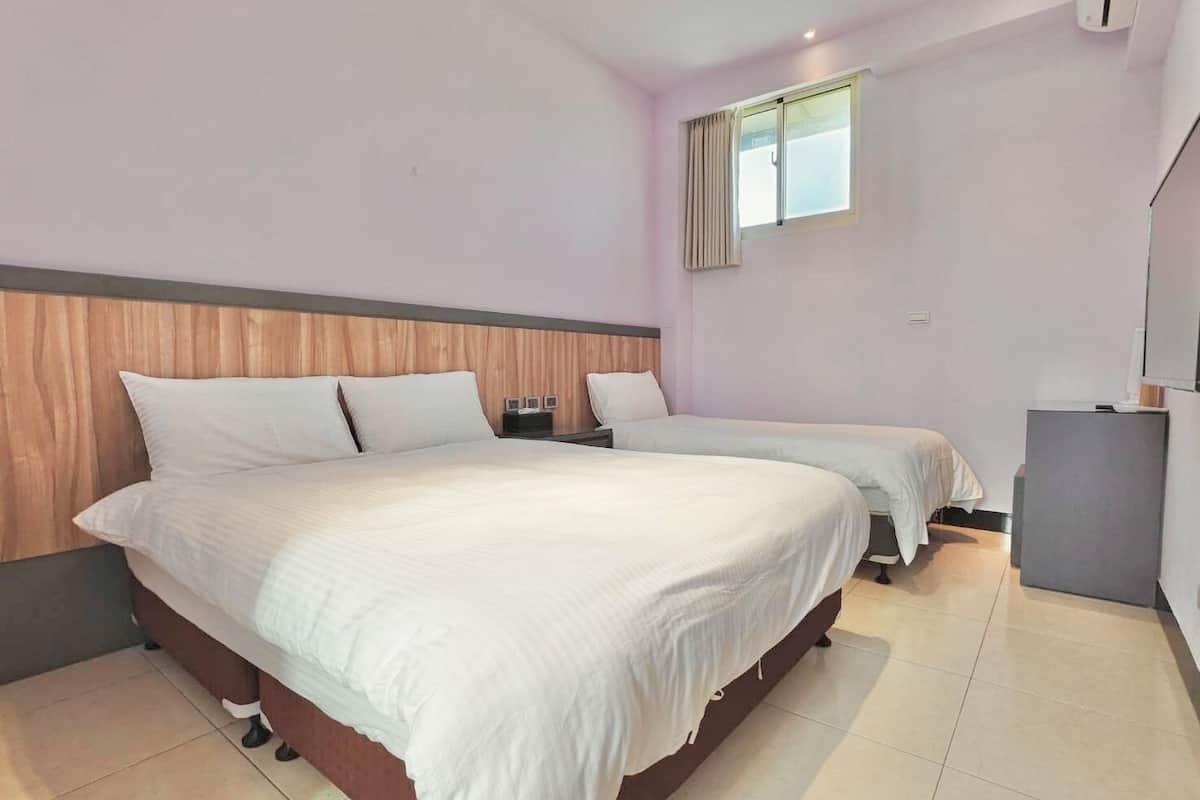 Une chambre d’hôtel avec deux lits, une tête de lit en bois, une petite fenêtre et un téléviseur.