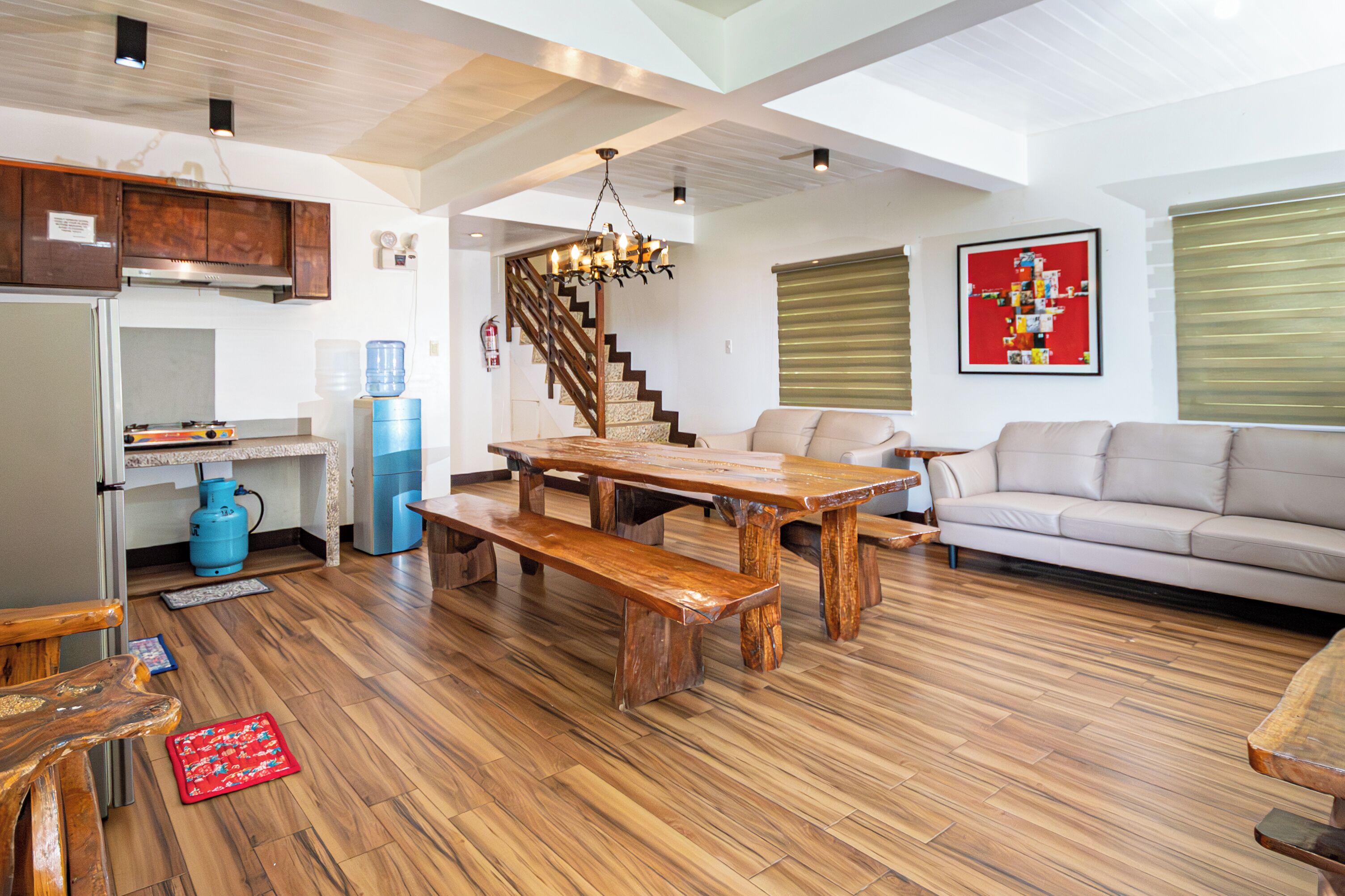 A spacious living area with a wooden dining table, a sofa, and a staircase leading to an upper level.