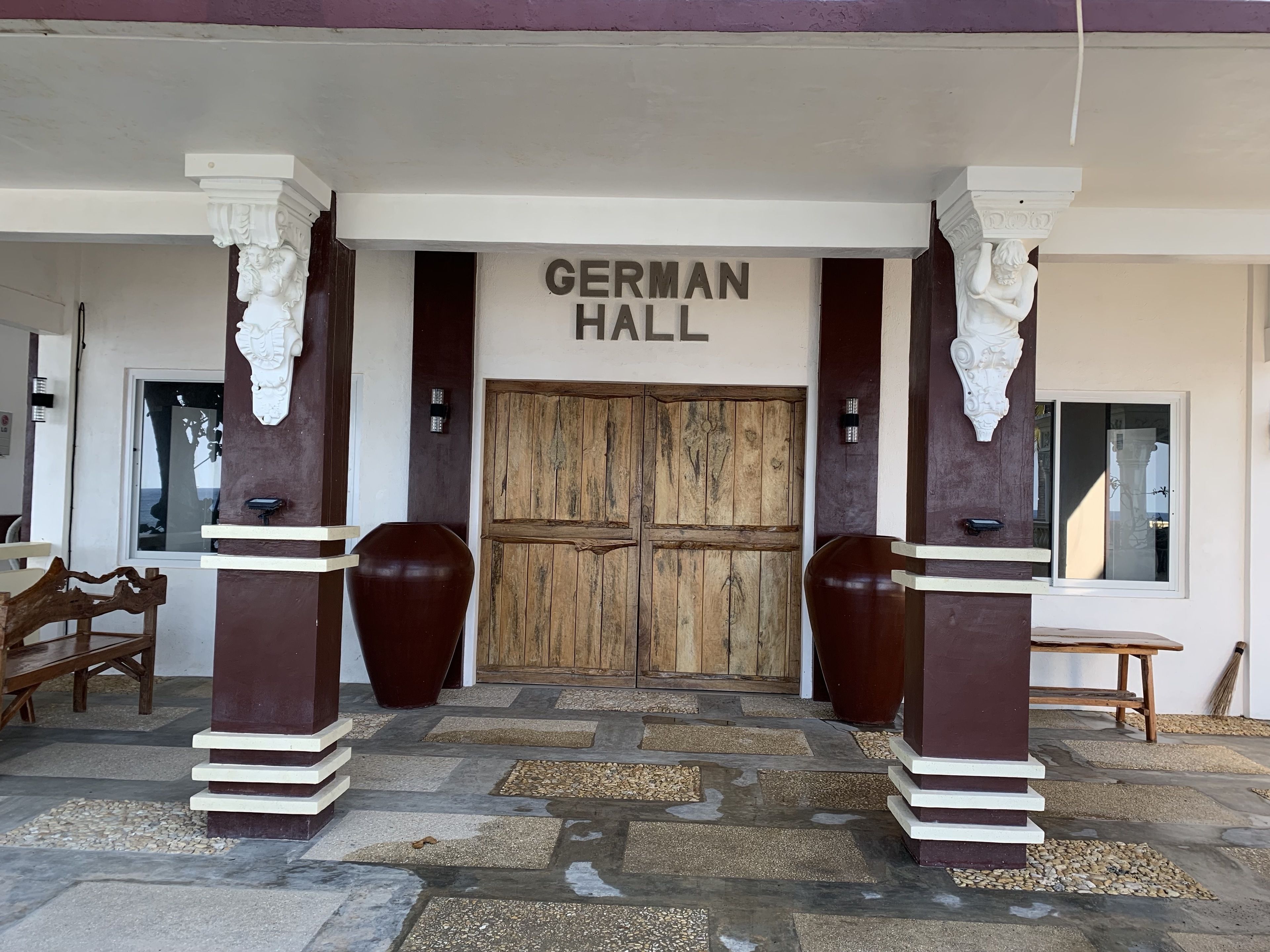 The entrance to German Hall with a wooden door, two large vases, and a stone-tiled entrance.