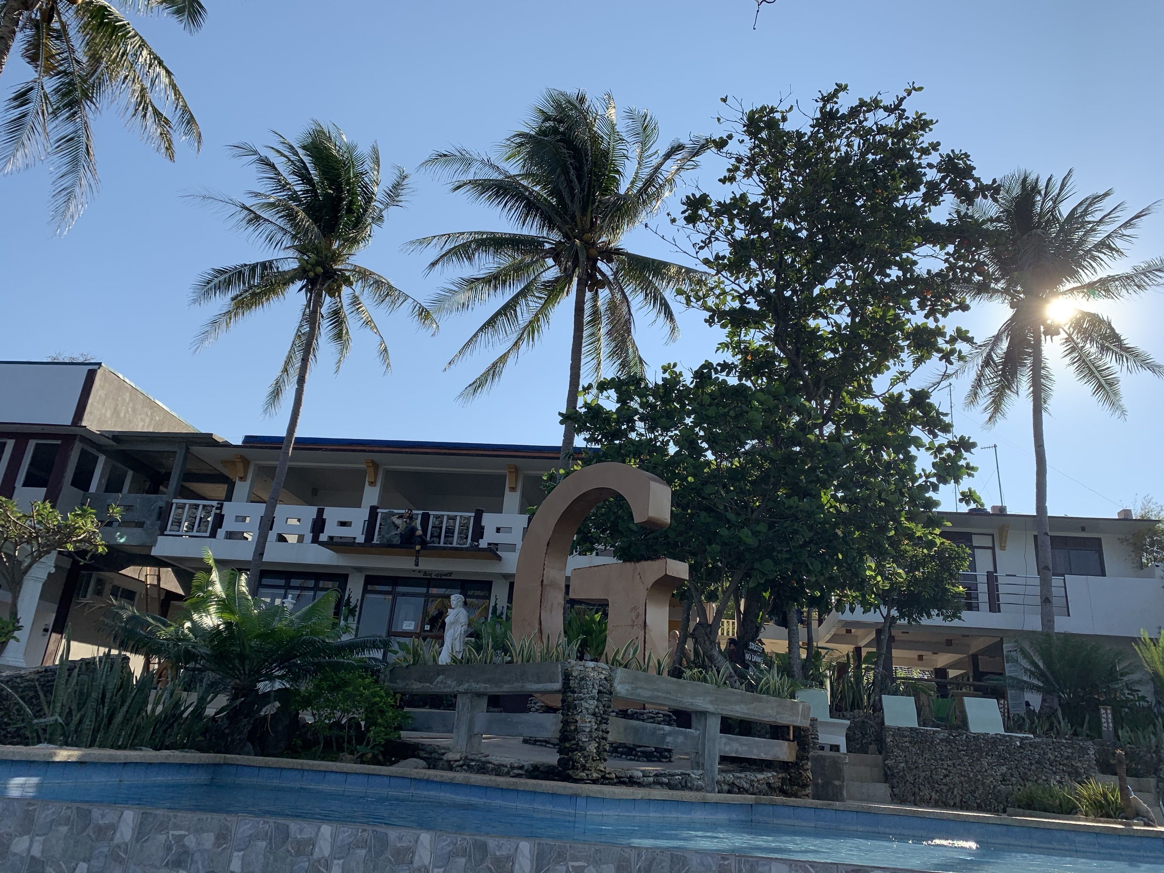 A hotel with a pool, palm trees, and a statue.
